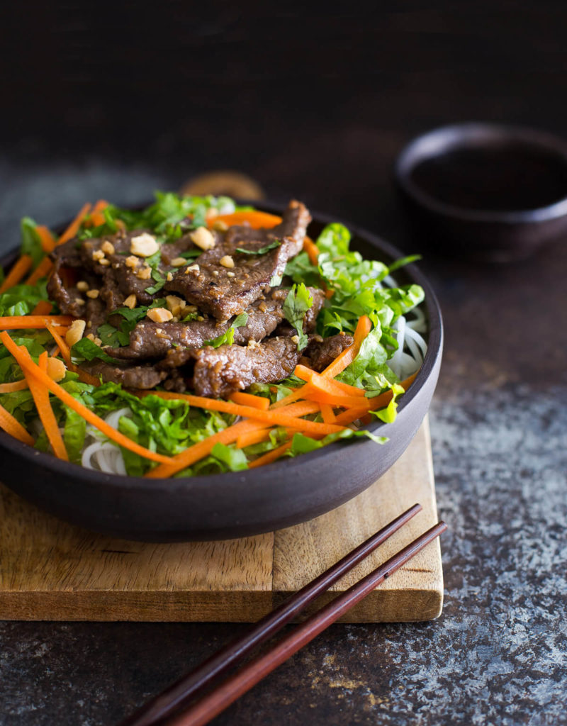 Bowl of Vietnamese lemongrass beef with noodles, lettuce, and shredded carrots.