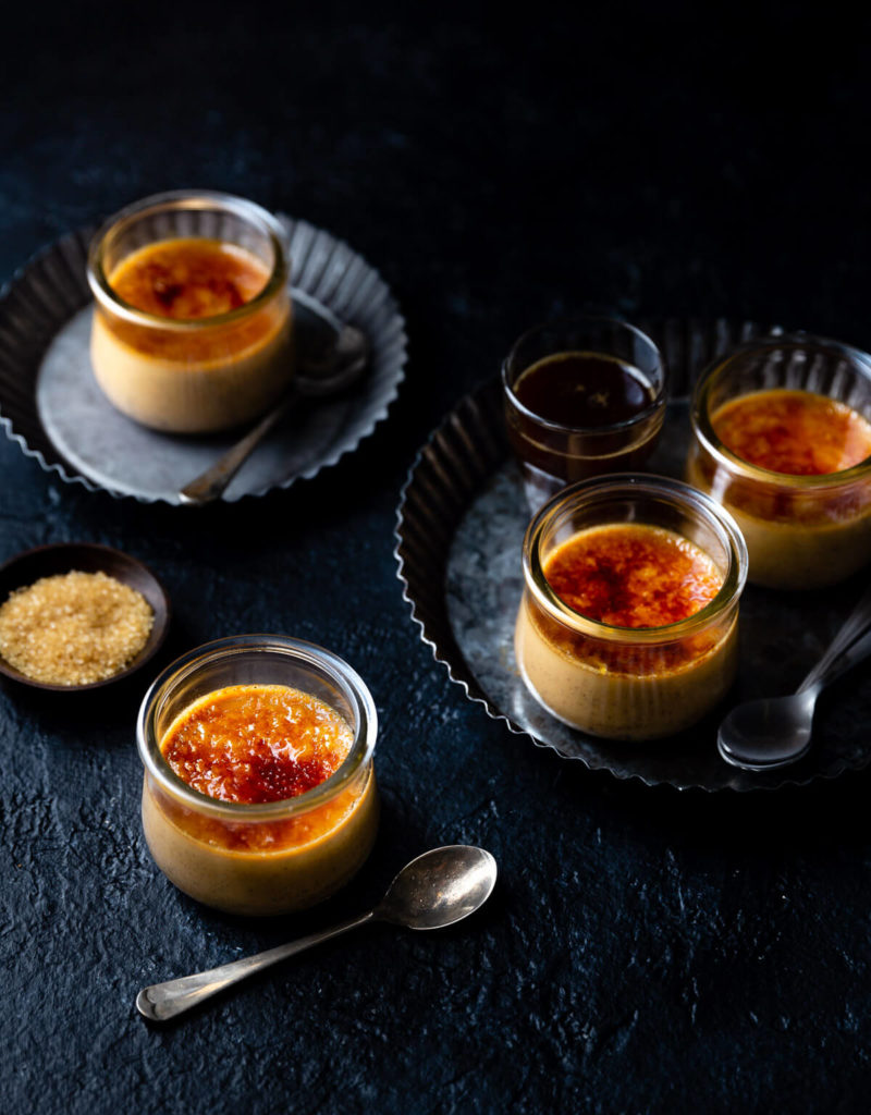 Several ramekins of coffee crème brûlée on pewter plates.