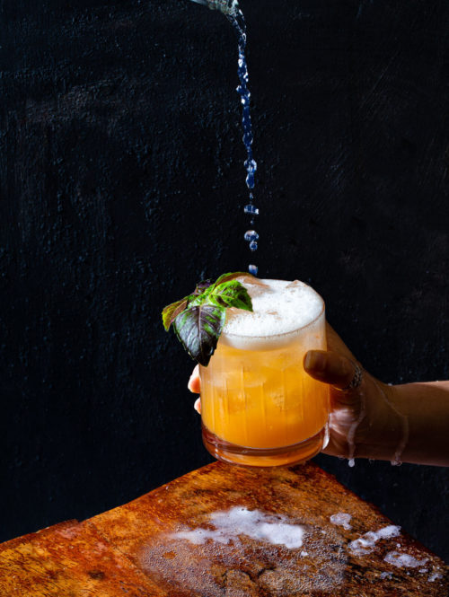 Tonic water being poured into a basil-peach shrub cocktail.