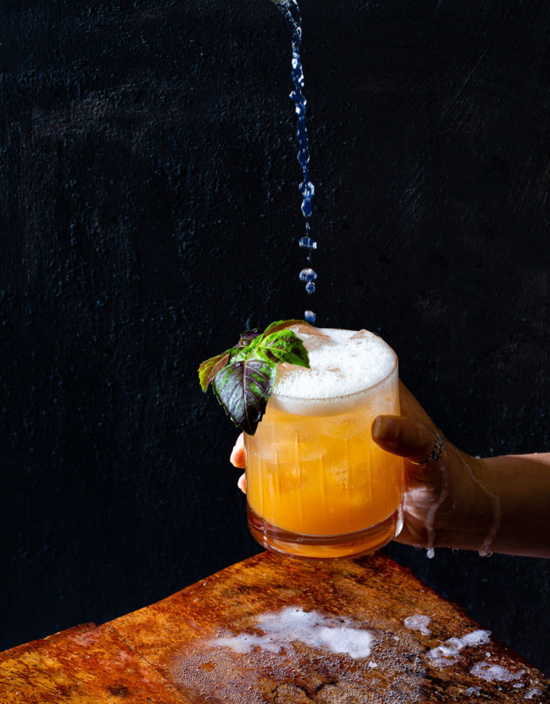 Tonic water being poured into a basil-peach shrub cocktail.