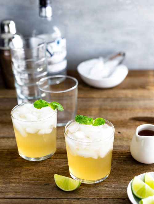 Two glasses of (Texas) Moscow Mule cocktail garnished with mint leaves on a dark wood table.
