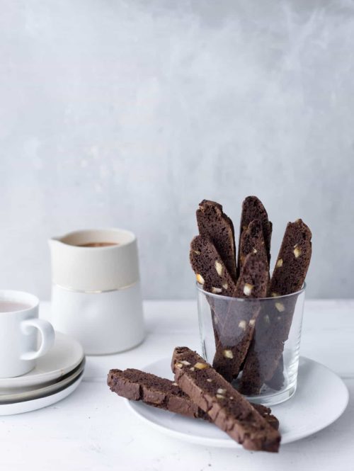 Several pieces of chocolate-orange biscotti in a glass served with a mug of hot chocolate.