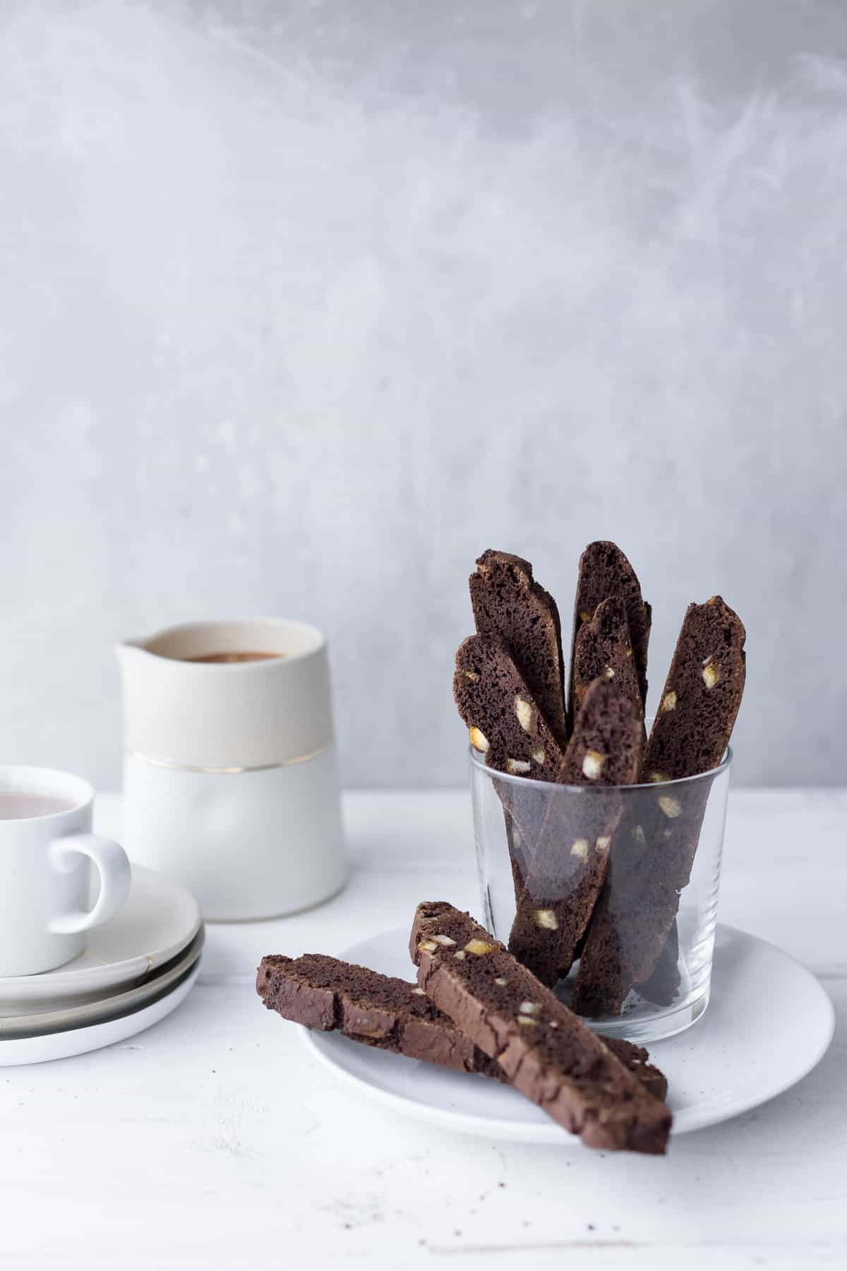 Several pieces of chocolate-orange biscotti in a glass served with a mug of hot chocolate.