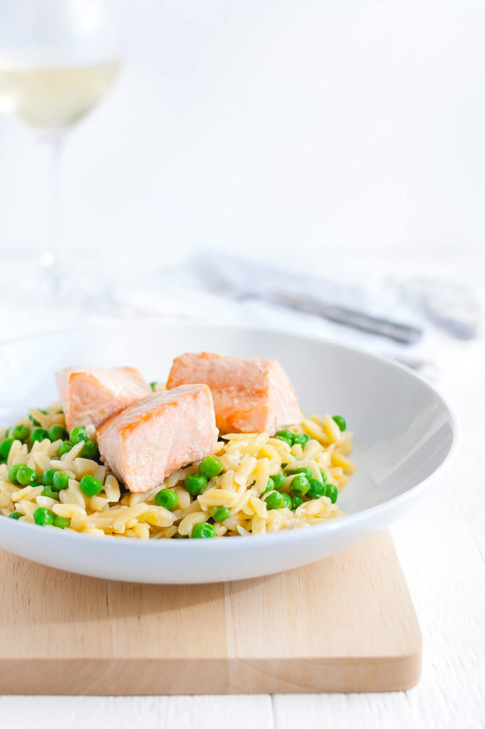 Plate of parmesan orzo with salmon and peas in a white bowl.