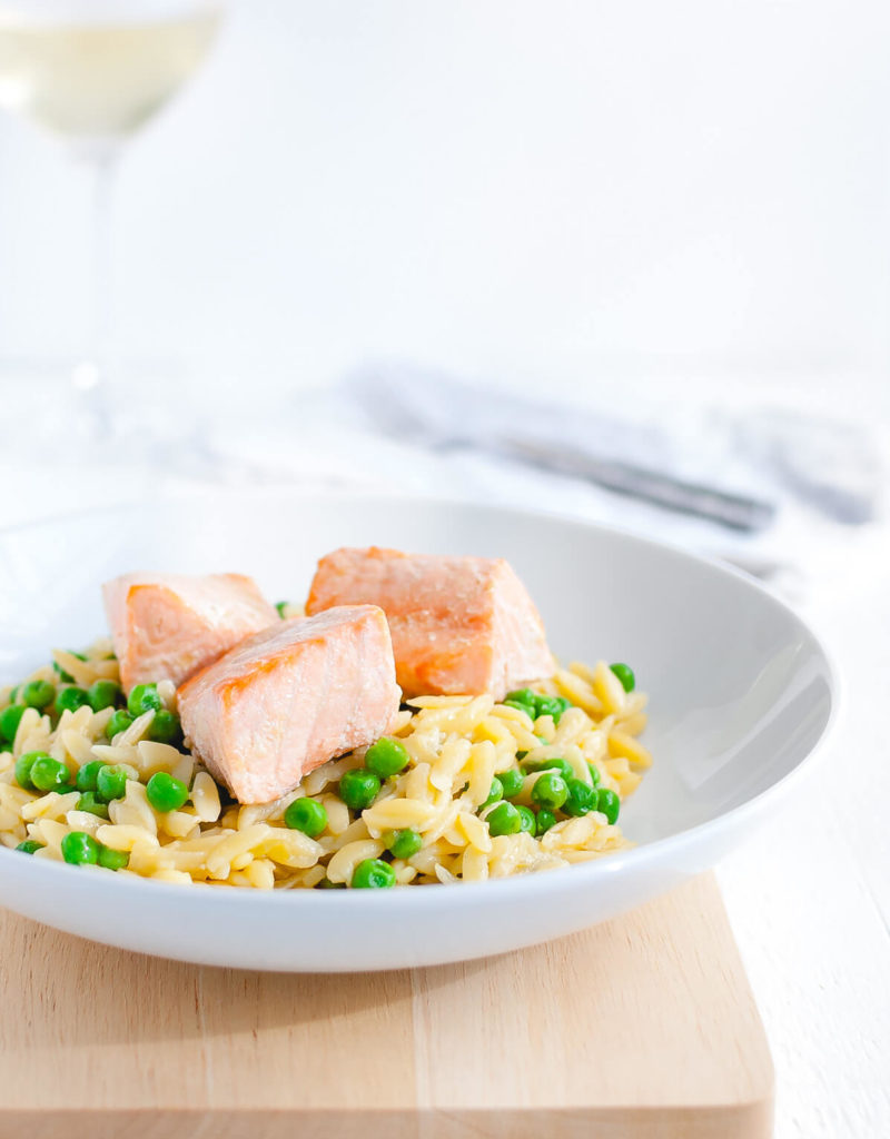 Plate of parmesan orzo with salmon and peas in a white bowl.