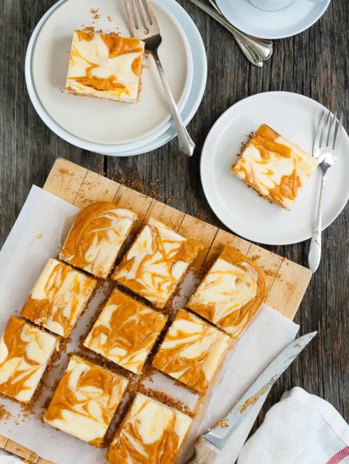 Several slices of marbled pumpkin cheesecake bars on a serving board plus two slices on plates.
