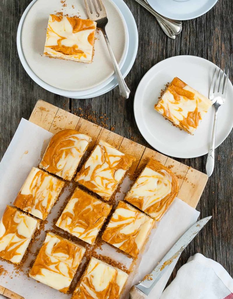 Several slices of marbled pumpkin cheesecake bars on a serving board plus two slices on plates.