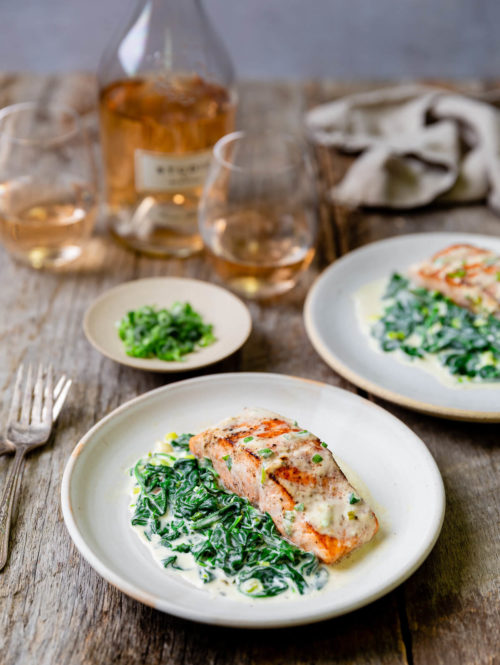 Two plates of pan seared salmon with creamed spinach on the side.