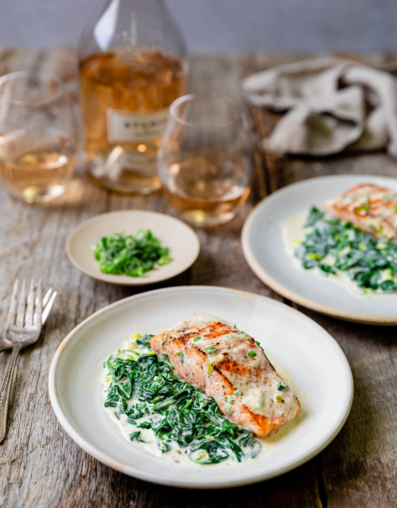 Two plates of pan seared salmon with creamed spinach on the side.