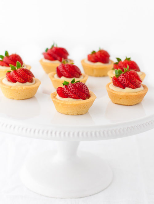 Several mini strawberry tartlets on a white cake stand.