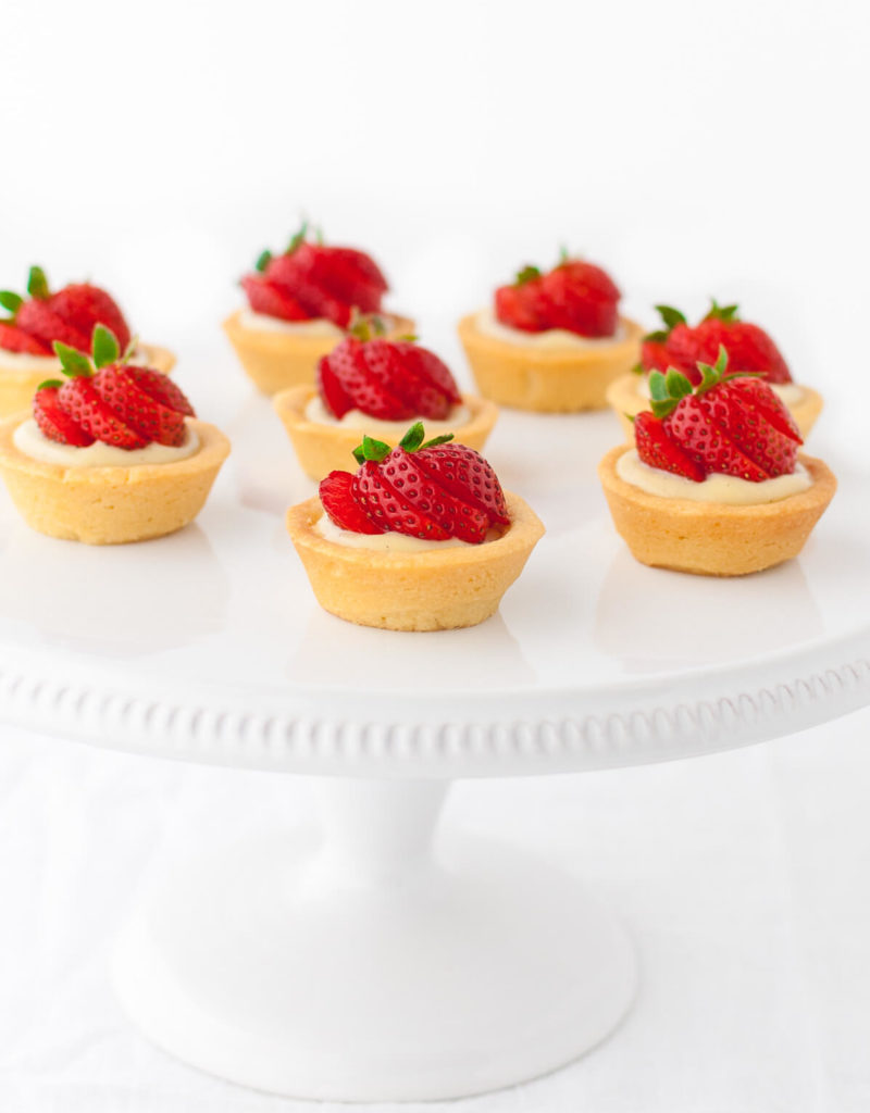Several mini strawberry tartlets on a white cake stand.