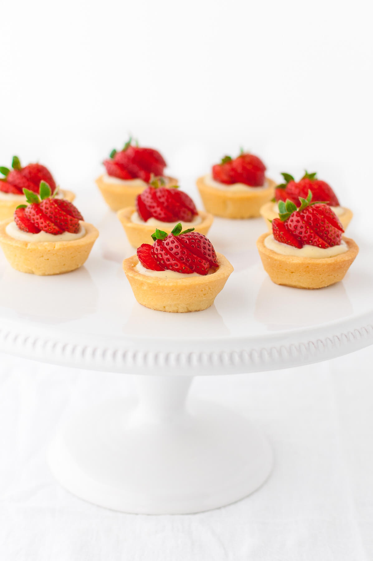 Several mini strawberry tartlets on a white cake stand.