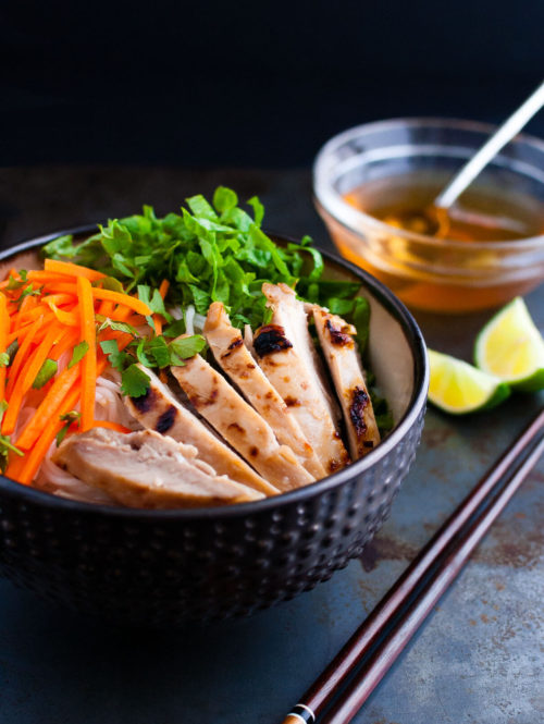 Vietnamese noodles with marinated grilled chicken in a bowl served with fresh lettuce, herbs, and fish sauce.
