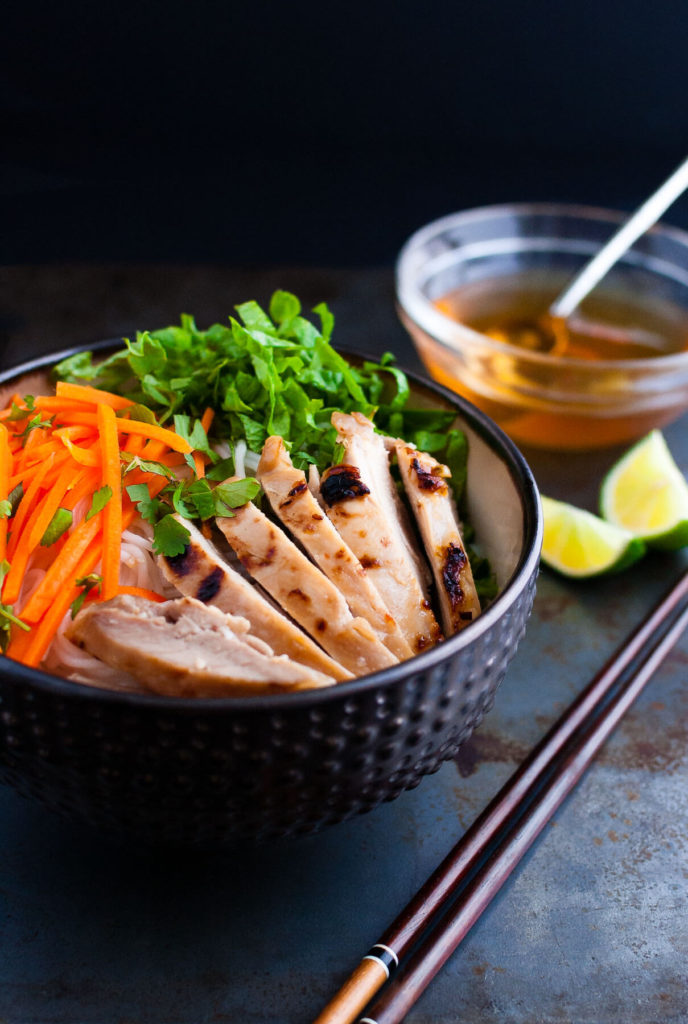 Vietnamese noodles with marinated grilled chicken in a bowl served with fresh lettuce, herbs, and fish sauce.