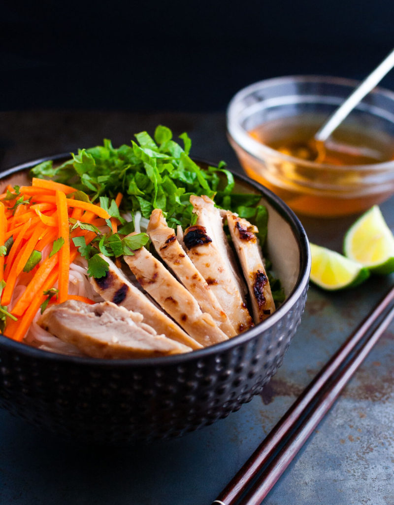 Vietnamese noodles with marinated grilled chicken in a bowl served with fresh lettuce, herbs, and fish sauce.