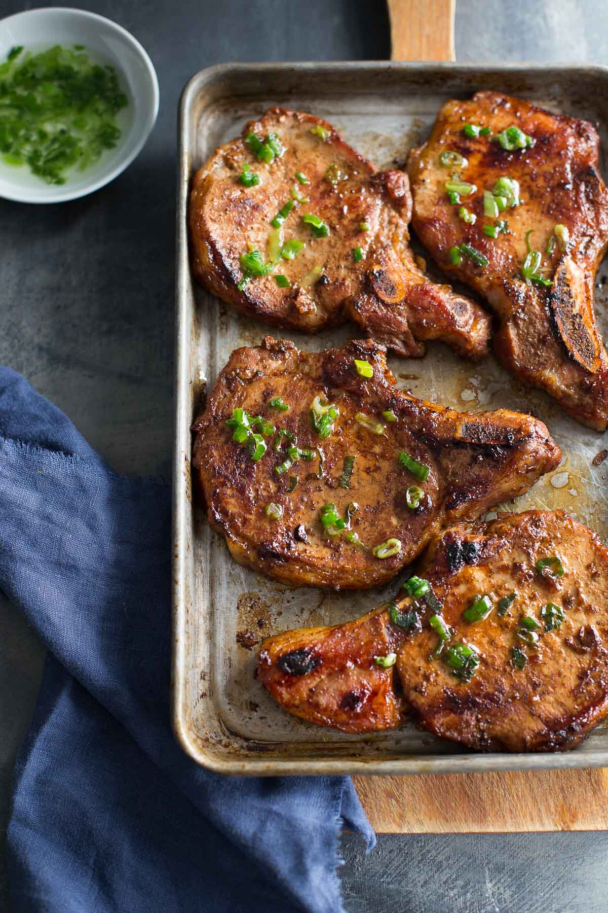 Top view of sheet pan with Vietnamese pork chops, dish of scallion oil, and blue napkin.