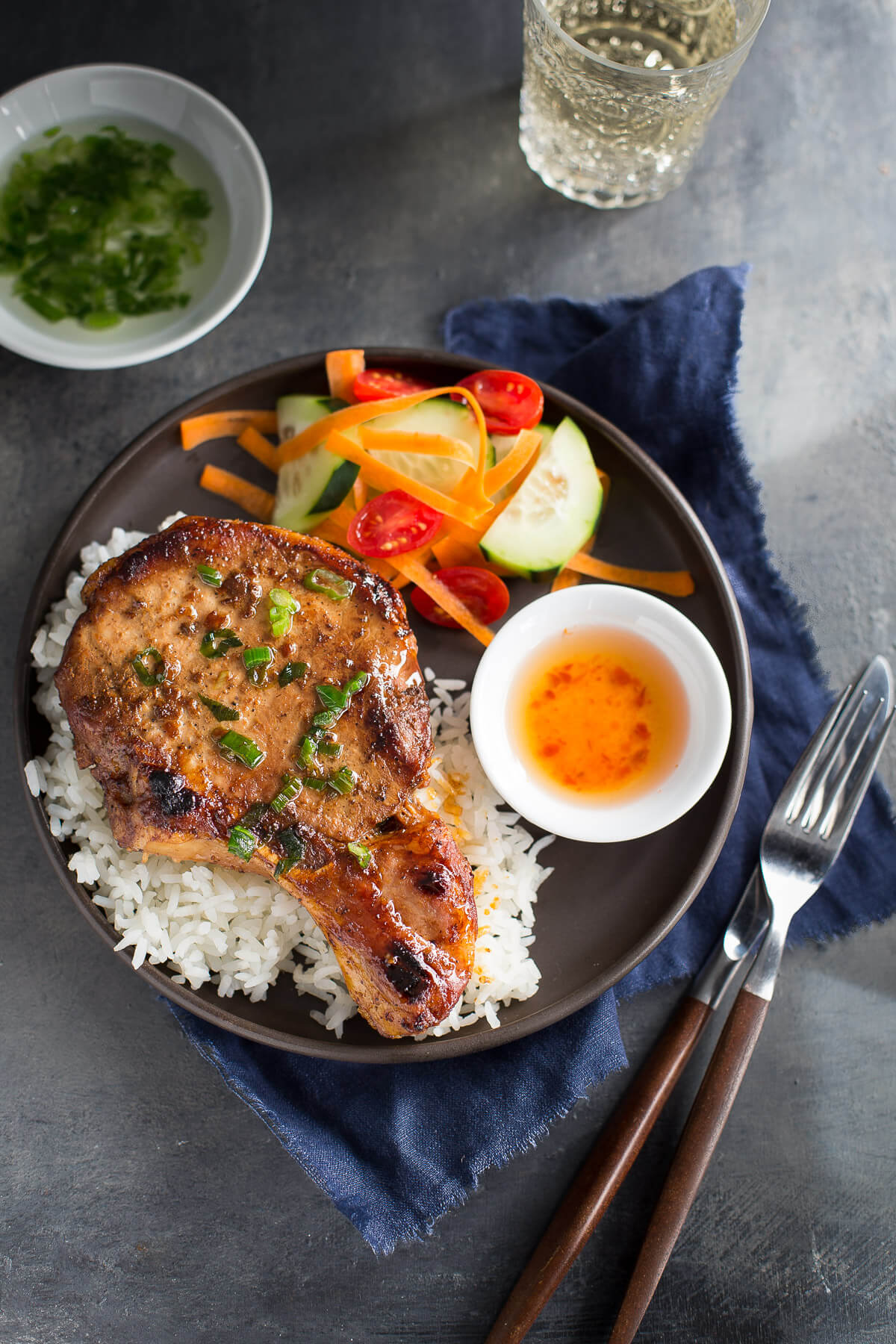 Top view of Vietnamese pork chop on jasmine rice, cucumber salad, and fish sauce on a brown plate.