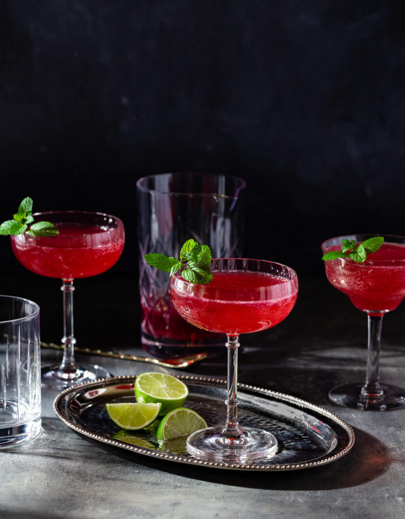 Several glasses of sparkling ginger pomegranate mocktail on a dark table.