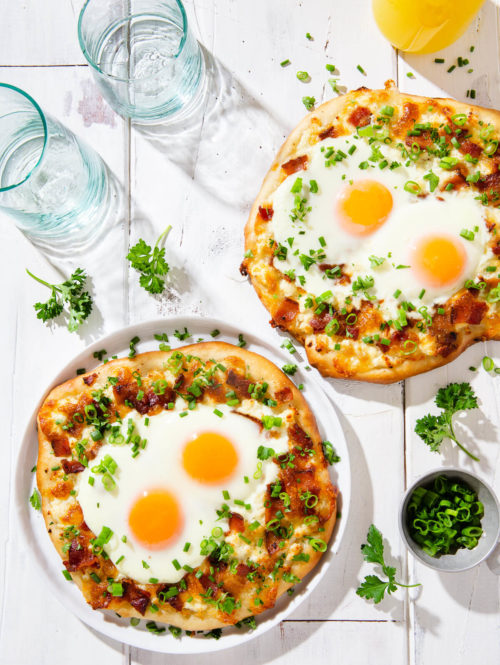 Overhead view of two breakfast pizzas on a white board.
