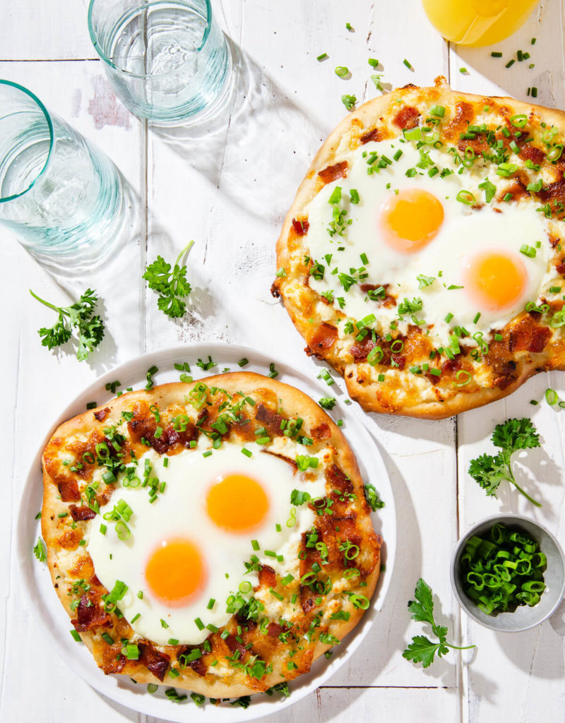 Overhead view of two breakfast pizzas on a white board.