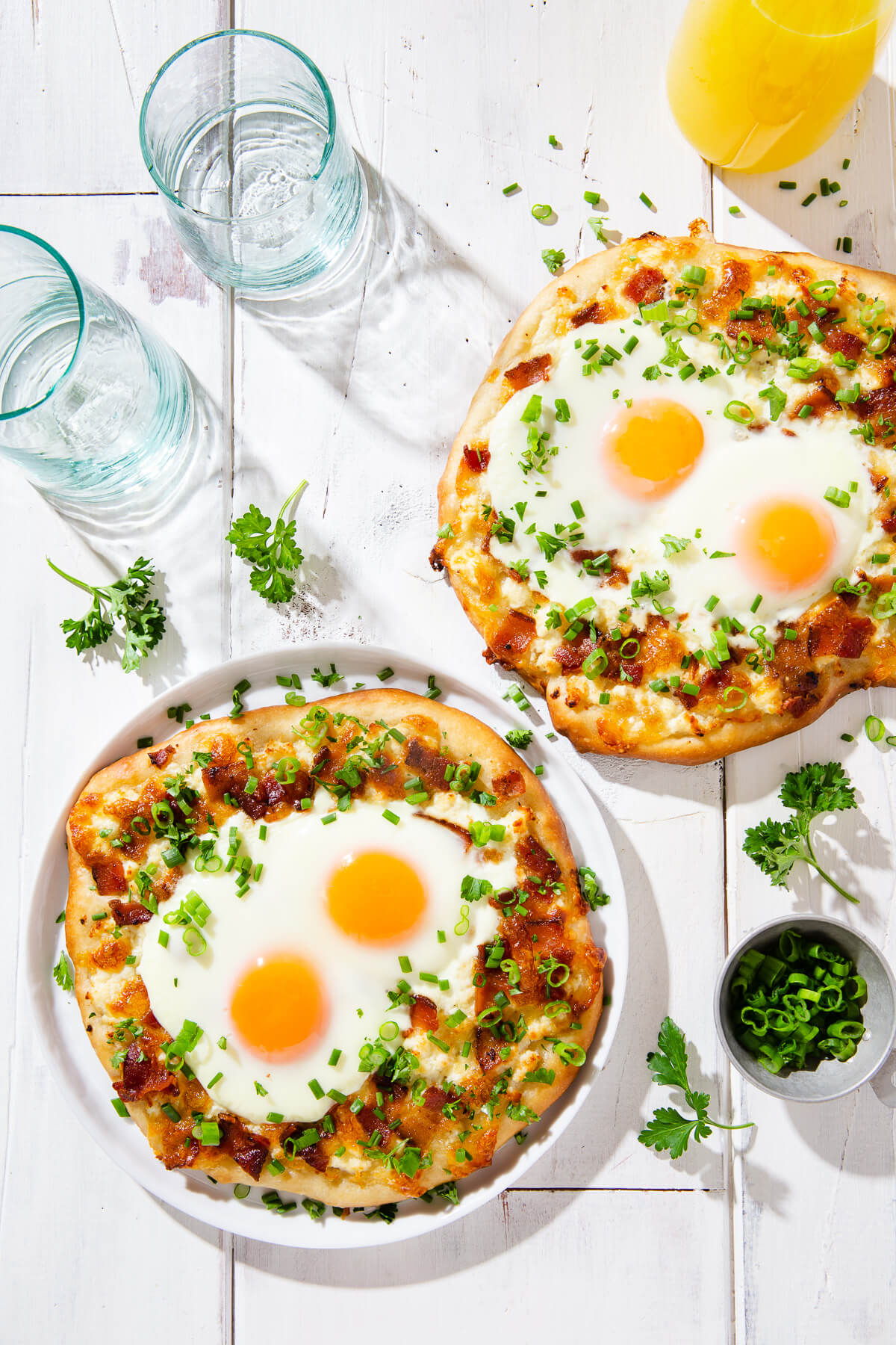 Overhead view of two breakfast pizzas on a white board.
