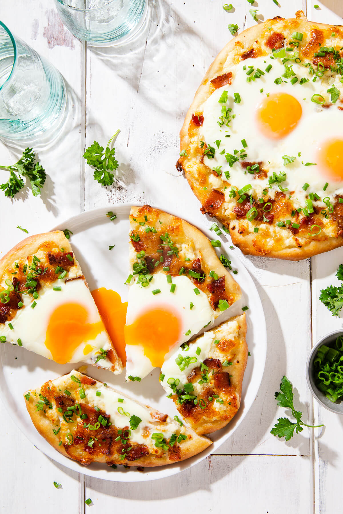 Overhead view of two breakfast pizzas on a white board.