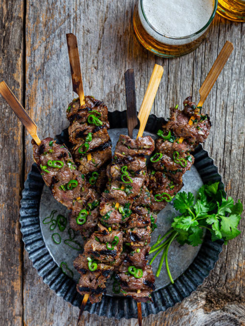 Overhead view of several lemongrass beef skewers on a metal serving dish.