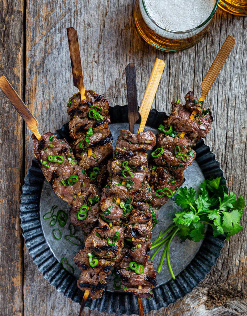 Overhead view of several lemongrass beef skewers on a metal serving dish.
