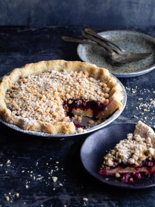 A lemon-blueberry streusel pie with a slice taken out next to a slice of pie on a plate.