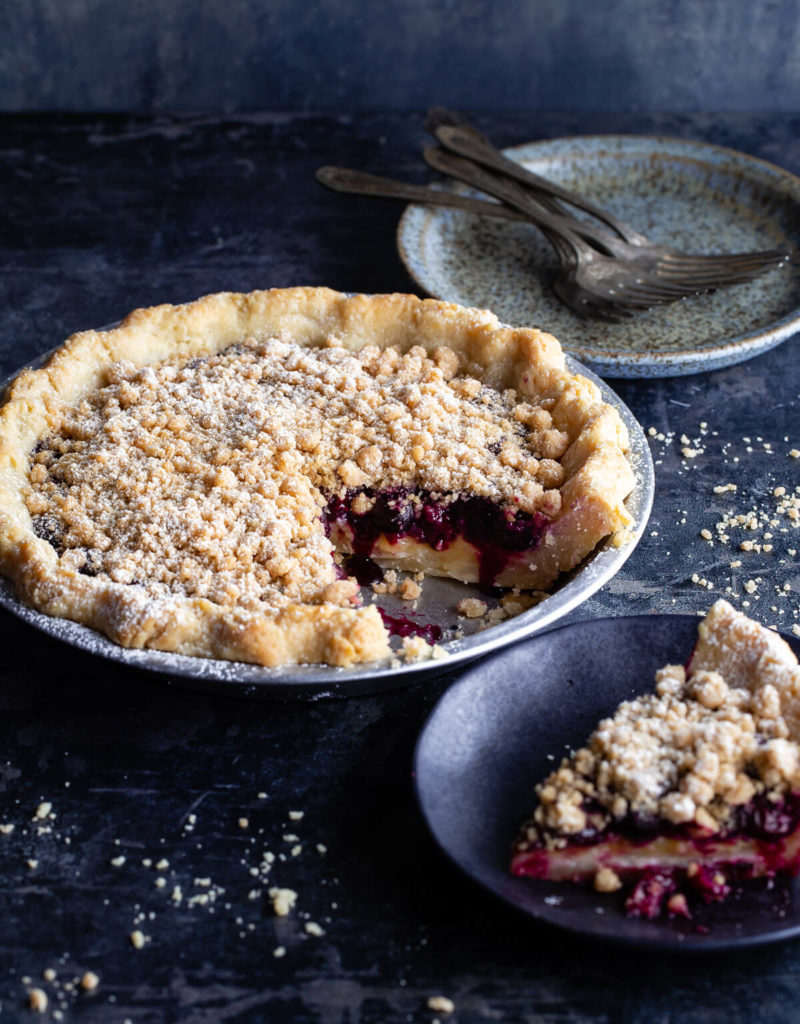 A lemon-blueberry streusel pie with a slice taken out next to a slice of pie on a plate.