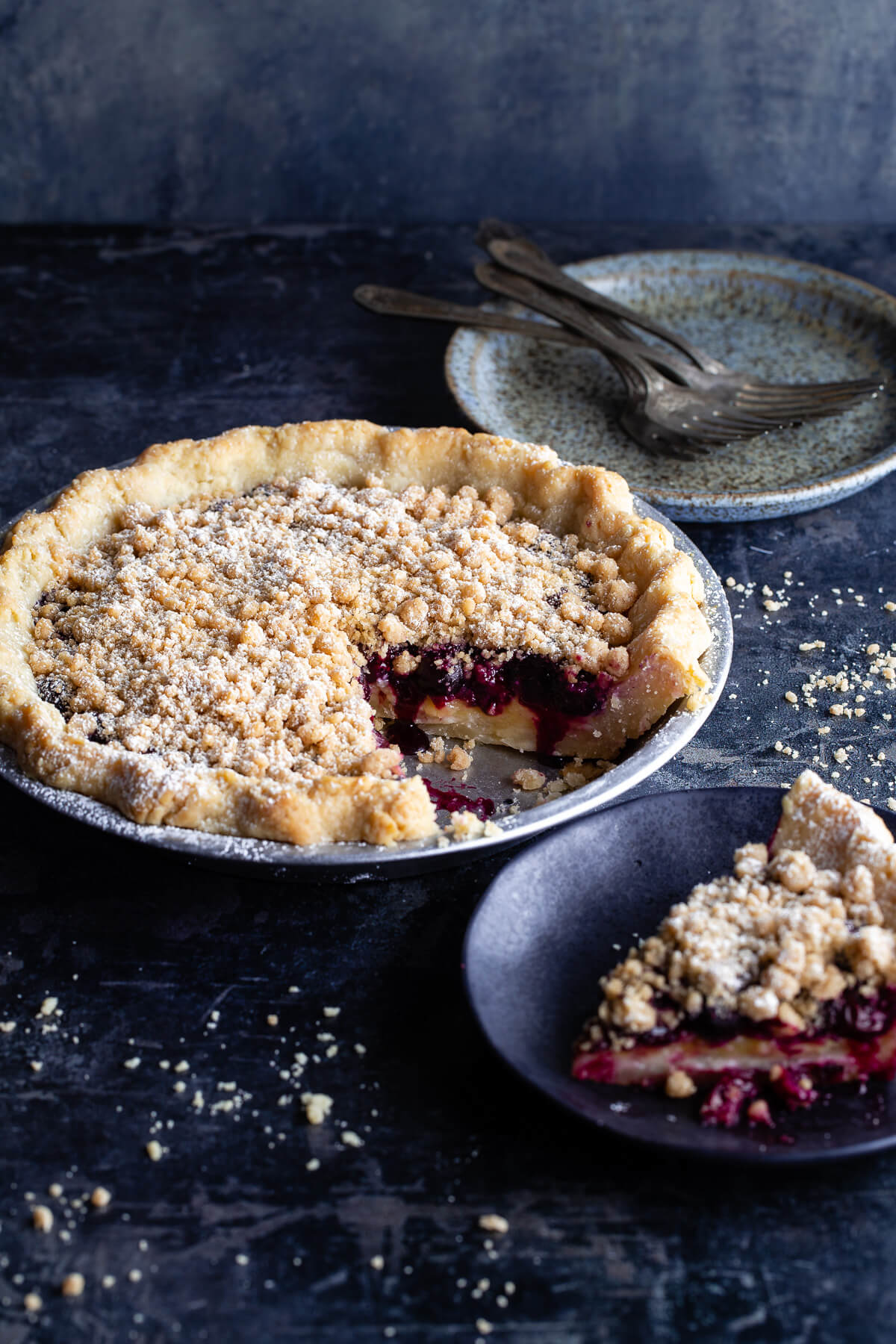 A lemon-blueberry streusel pie with a slice taken out next to a slice of pie on a plate. 