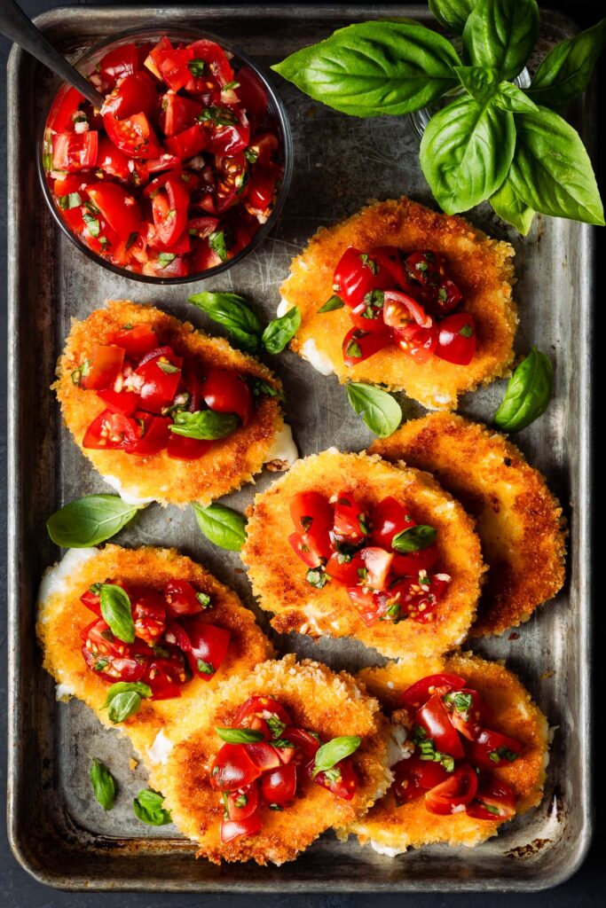 Overhead shot of fried mozzarella slices topped with tomatoes and basil.