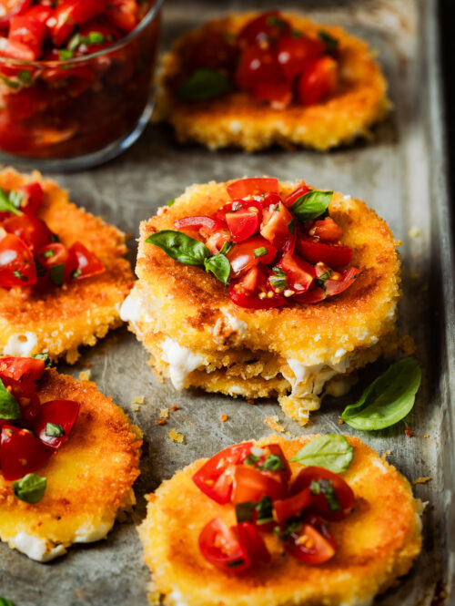 Stack of fried mozzarella slices topped with tomatoes and basil.