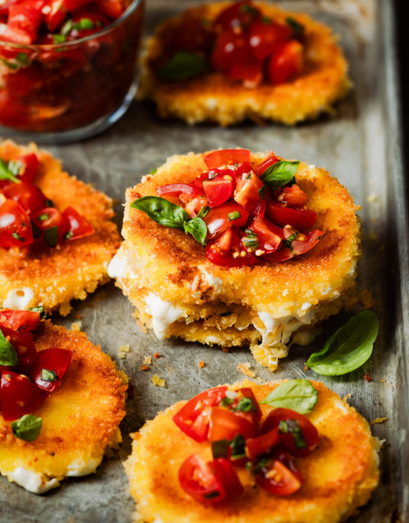 Stack of fried mozzarella slices topped with tomatoes and basil.