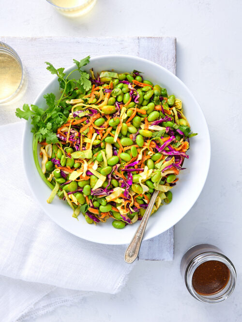 Big bowl of edamame salad with jar of miso dressing.