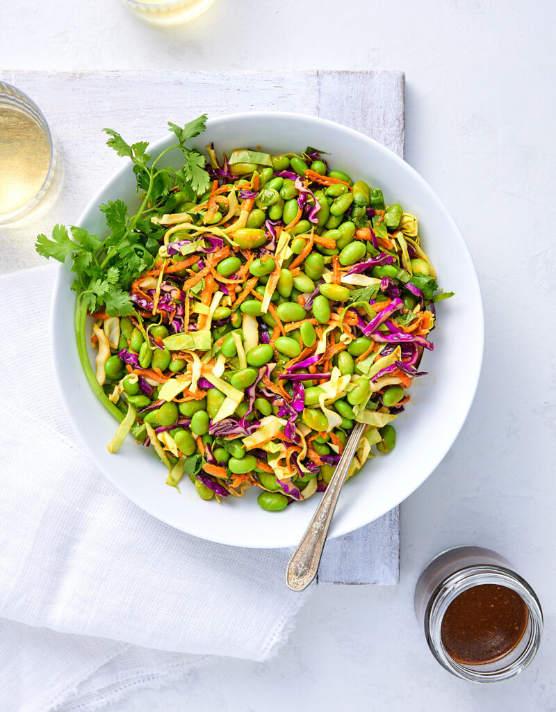 Big bowl of edamame salad with jar of miso dressing.