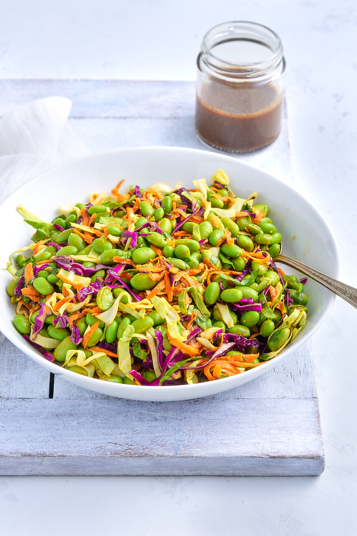 Bowl of edamame salad and jar of miso dressing on a white board.