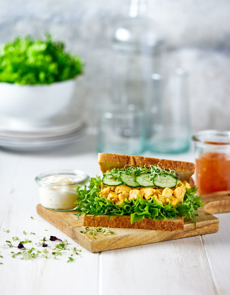 Chicken salad sandwich being assembled on a wooden board.