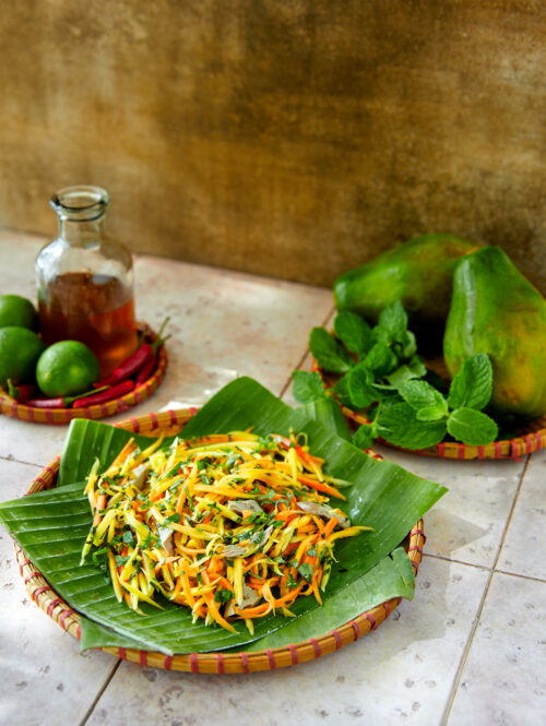 Papaya salad on some banana leaves with some mint and papaya in the background.