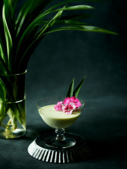 Pandan panna cotta in a short stem glass with pandan leaves in background.