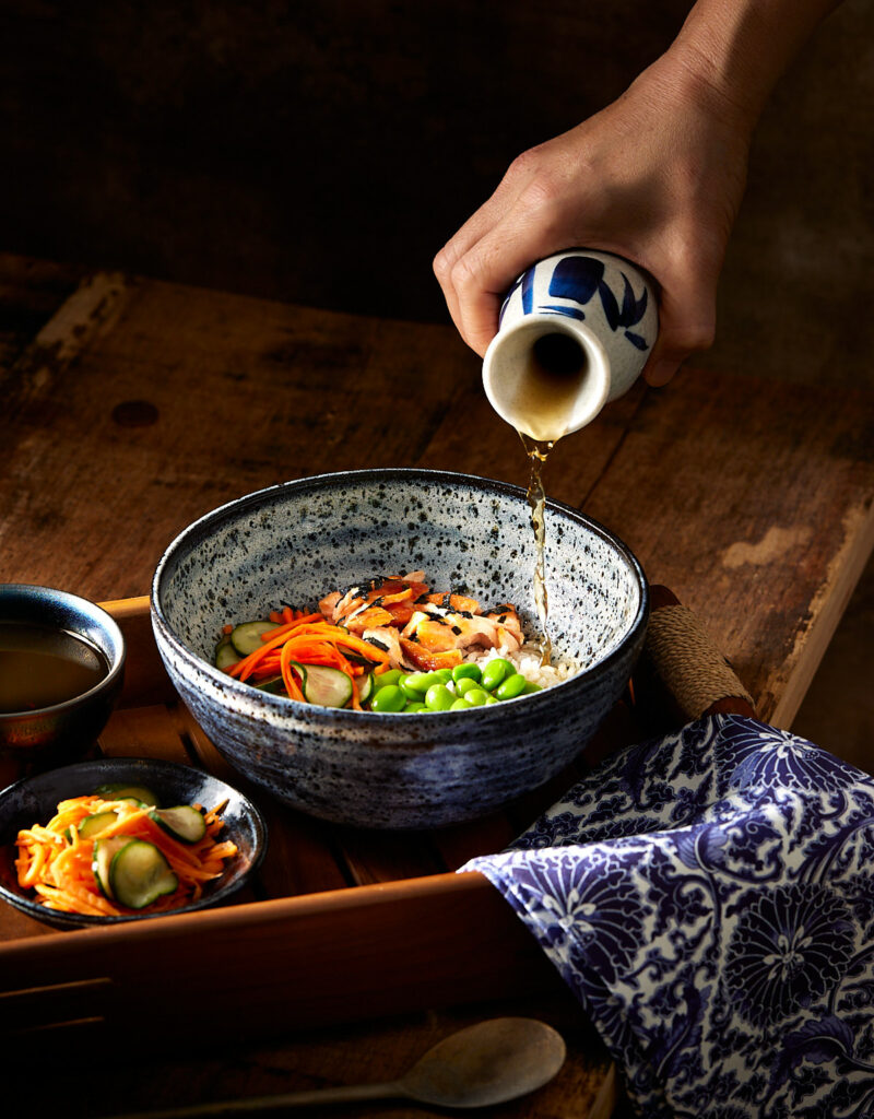 Dashi broth being poured into a bowl of salmon and rice.