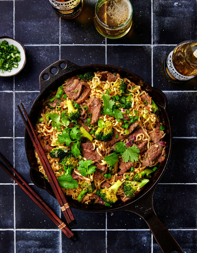 Top down view of skillet with beef noodles and broccoli.
