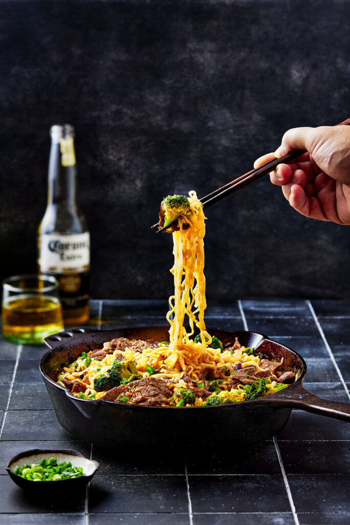 Noodles being lifted from skillet with chopsticks.