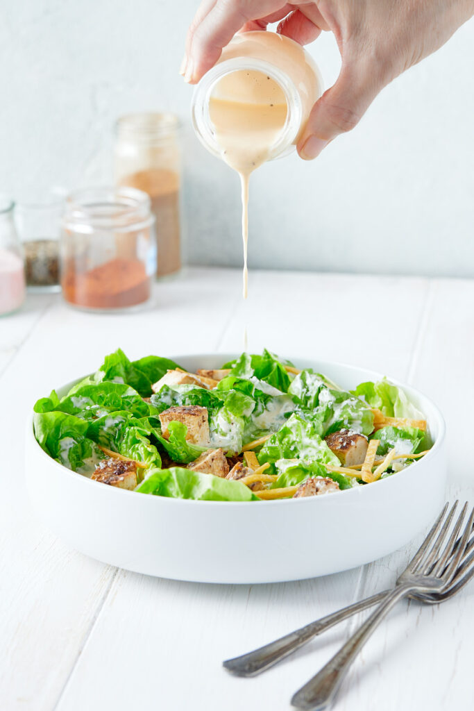 Dressing being poured over chicken caesar salad.