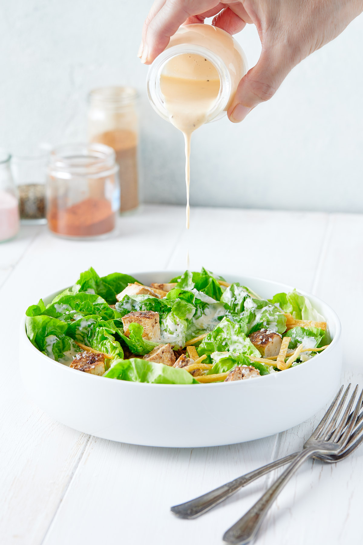 Dressing being poured over chicken caesar salad.