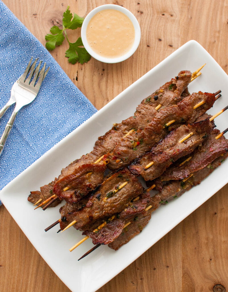 Overhead view of skewers of beef satay on a white plate.