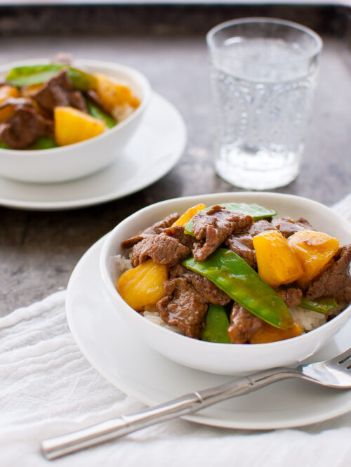 Beef, pineapple, and snow peas stir-fry in a white bowl.