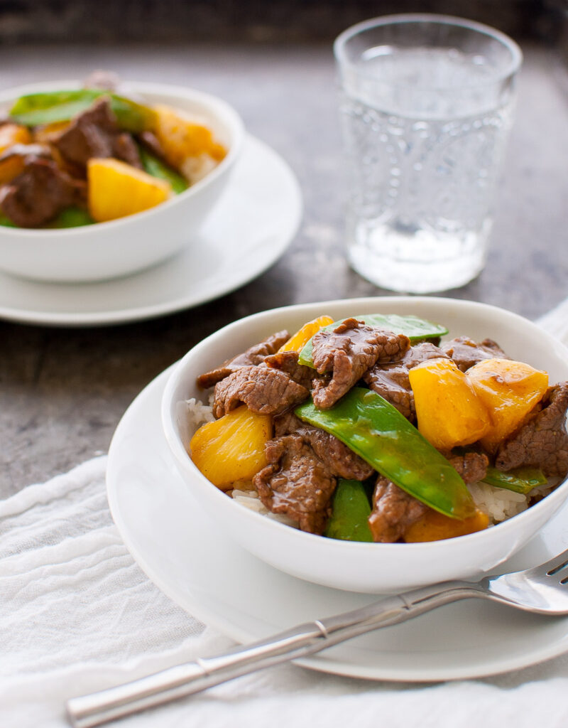 Beef, pineapple, and snow peas stir-fry in a white bowl.