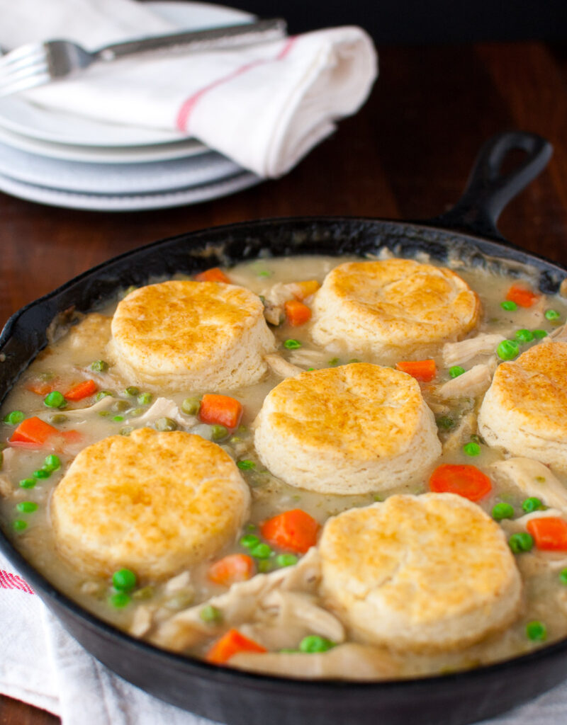 Chicken pot pie topped with biscuits in a cast iron skillet.