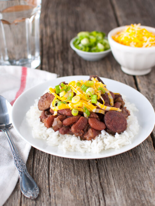 Plate of red beans and rice next to bowl of grated cheese and bowl of green onions.